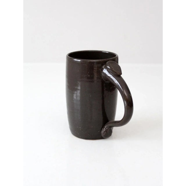 This handmade vintage studio pottery mug is finished in a deep brown glaze with a glossy, earthen richness. Its tall...