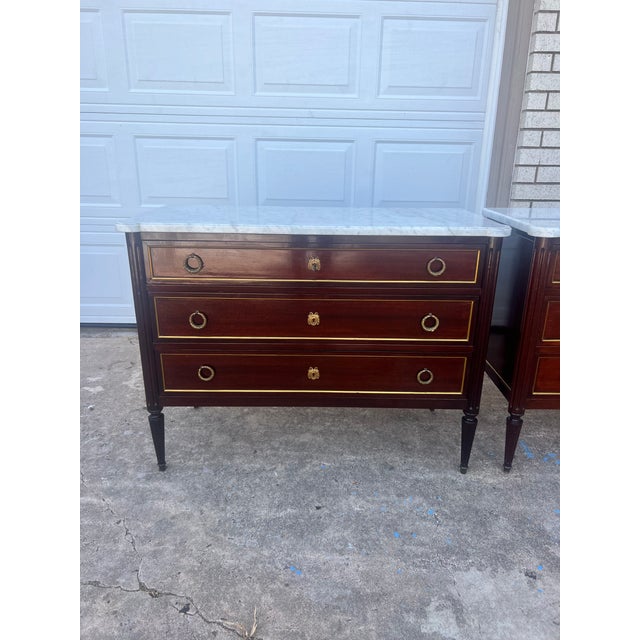 An elegant pair of 19th-century Louis XVI-style commodes, featuring luxurious Carrara marble tops above beautifully...