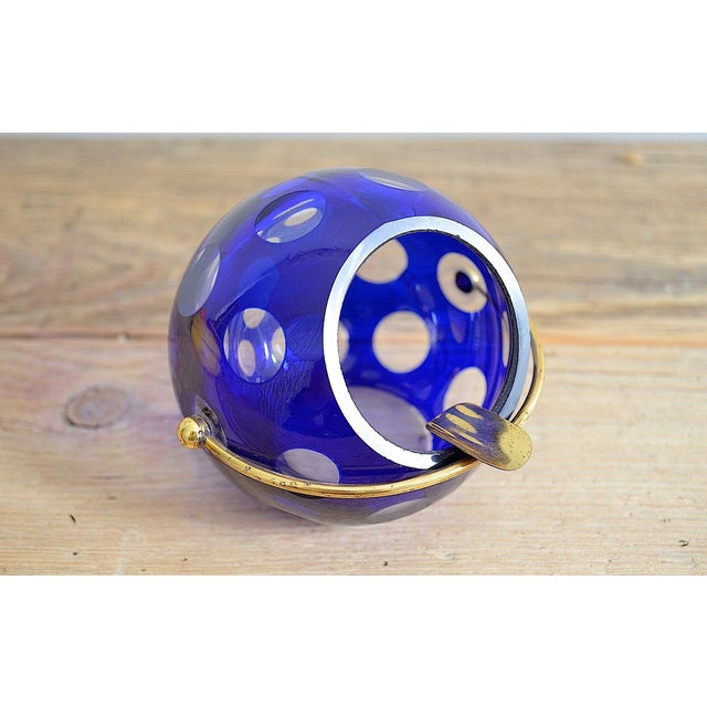 Mid-century spherical ashtray with a tilting cigarette rest, made of brass. The ashtray is made of blue overlaid glass and...