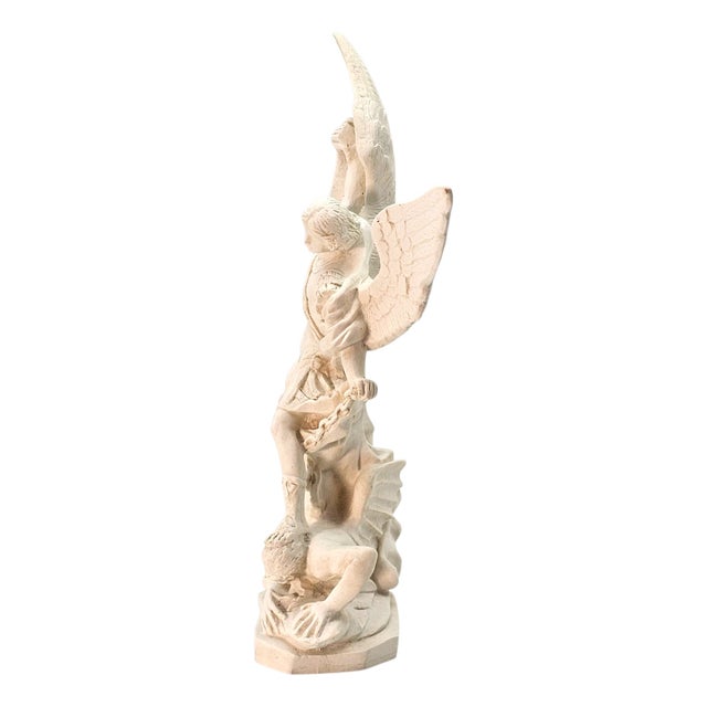 A sculptural depiction of St. Michael the Archangel in a dynamic moment of triumph, rendered in a marble-resin composite...