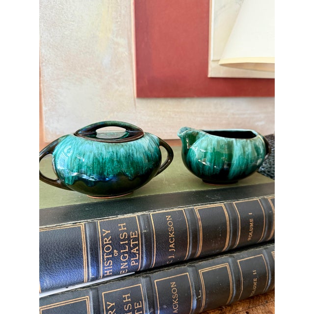 A striking mid-century Blue Mountain Pottery creamer and sugar bowl set in a deep emerald green drip glaze over a near-...