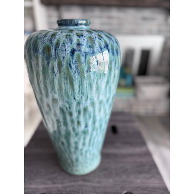 This sculptural ceramic vase features an elegantly tapered form and a luminous, high-gloss glaze inspired by the blues and...
