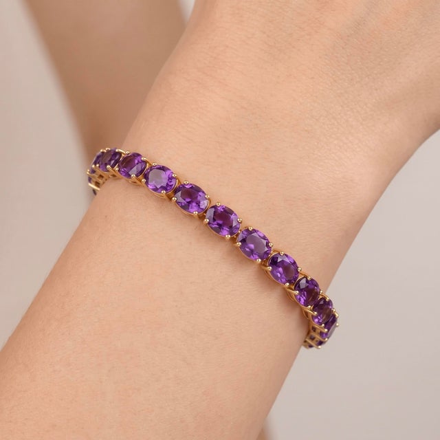 A stunning tennis bracelet showcasing a continuous row of vivid purple oval amethysts set in warm gold-tone sterling...