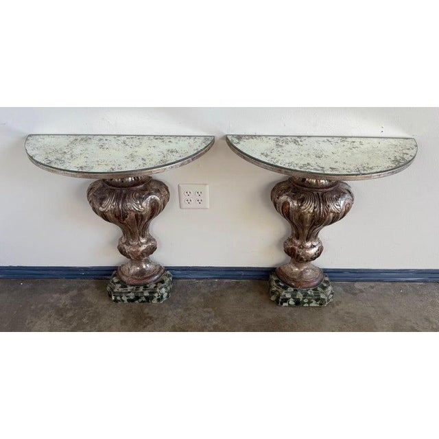 A dramatic and sculptural pair of Italian Baroque style wall-mounted console tables, richly finished in silver gilt with a...