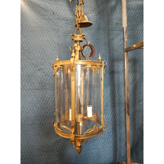 A classic French Louis XV–style brass hall lantern featuring a cylindrical form with gracefully curved glass panels and...