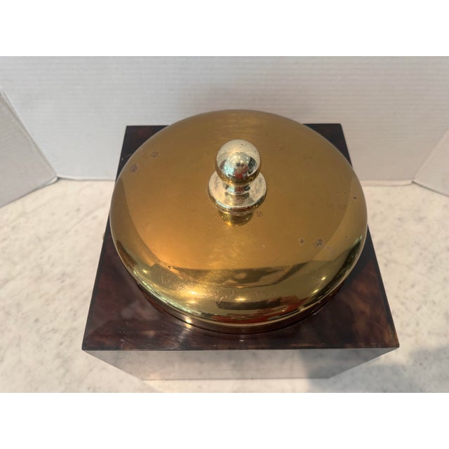 A faux tortoise shell ice bucket having a brass lid and brass rings on each side. Square in shape.