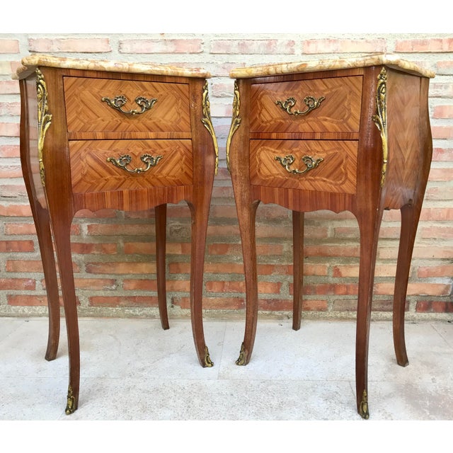 A pair of Antique French Louis XV Marquetry marble top nightstands. Subtle contours and scroll shapes are evident in the...
