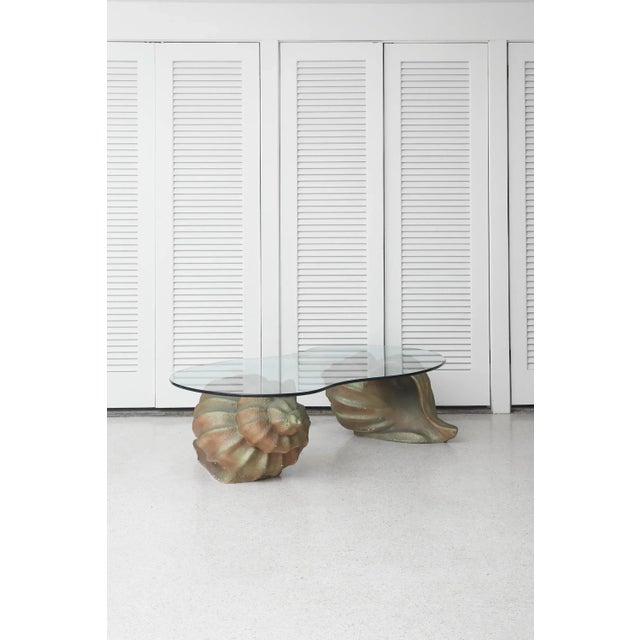 Large sculptural coffee table with two oversized conch shell bases supporting a biomorphic glass top. The design channels...