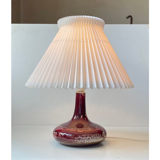 A stylish Danish table light featuring af stoneware base in deep red sang de boeuf glaze. It is accompanied by a white...