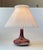 A stylish Danish table light featuring af stoneware base in deep red sang de boeuf glaze. It is accompanied by a white...