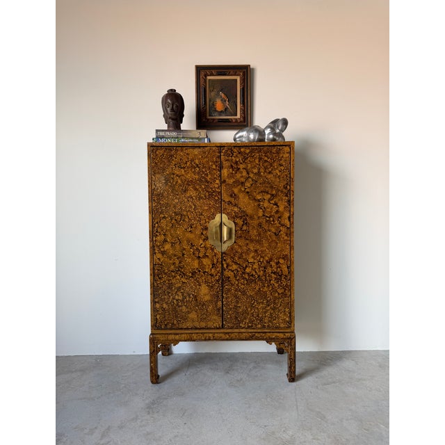 Beautiful Mid Century Hollywood Regency cabinet featuring a striking faux tortoiseshell finish, sculptural brass hardware....