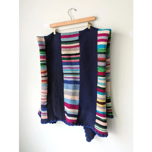 Vintage hand-knit wool throw blanket in colorful colorblock and stripe pattern with ruffled edge.