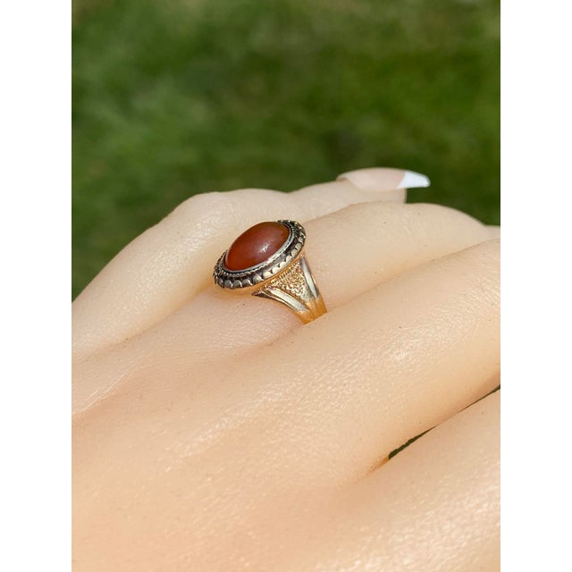 The Benson: Antique Carnelian Ring in Yellow Gold. The ring features a central oval cabochon of carnelian bezel set with a...
