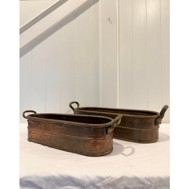 A beautiful pair of vintage copper planter troughs, featuring elongated oval forms with riveted brass loop handles. These...