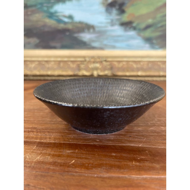 This handcrafted studio pottery bowl features a dark, iron-rich glaze and a finely textured surface with concentric,...