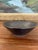 This handcrafted studio pottery bowl features a dark, iron-rich glaze and a finely textured surface with concentric,...