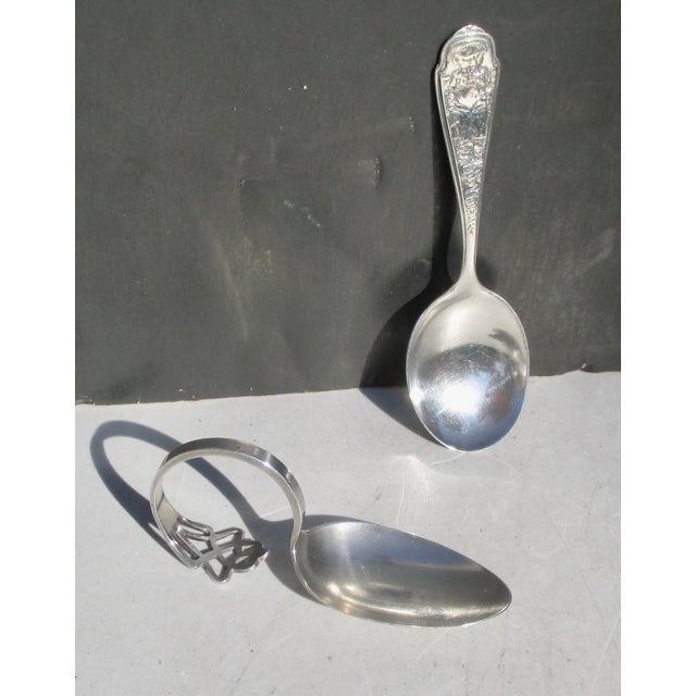 Two spoons for the baby. One short handle with a teddy bear design and the other with a pierced pattern on the curled...