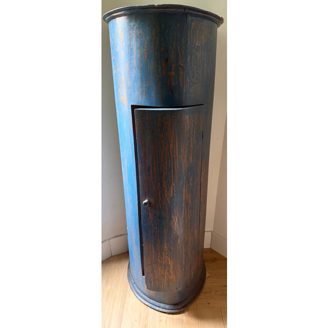 A rustic, single-door corner cabinet with a gently curved (bow) front, retaining its original blue painted surface over an...