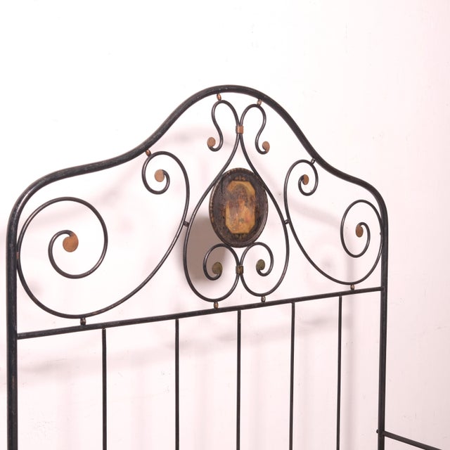 Beautiful wrought iron single bed, with decorated plates on the headboard and footboard, a female motif on the headboard...