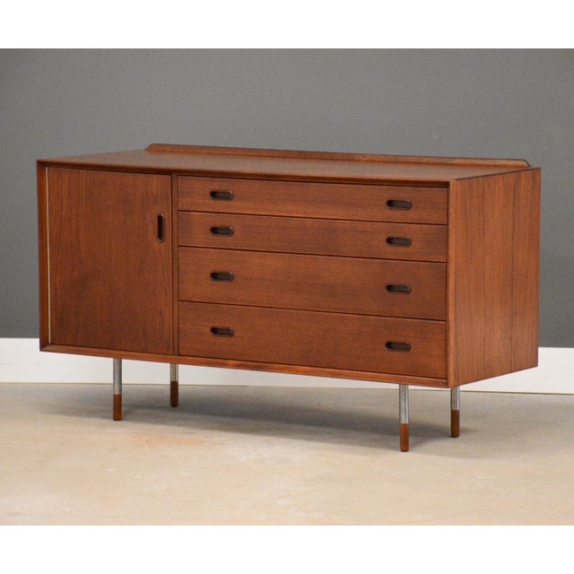 A mid century modern teak credenza with a swinging door, four drawers, and inset pulls designed by Arne Vodder for Sibast...
