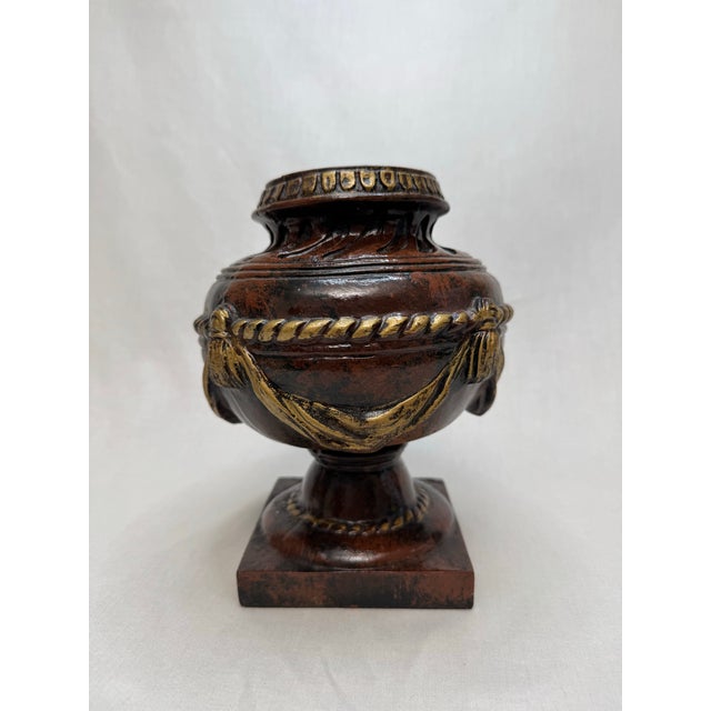 A faux marble deep chestnut brown and black colored glaze and gold painted accents highlight the exterior of this ceramic...