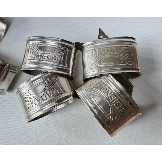 Complete set of sixteen vintage silver-tone metal napkin rings divided between embossed “Monsieur” and “Madame” designs....