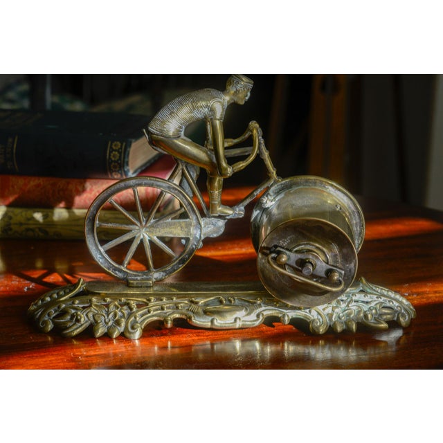 A rare novelty desk clock in the form of a Victorian cyclist on his bicycle, cast in brass, with the front wheel doubling...