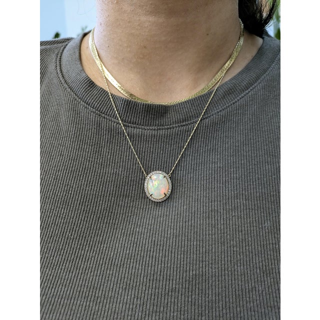 A luminous 6.36 carat Ethiopian opal takes center stage in this captivating pendant, cradled in a halo of natural, earth-...