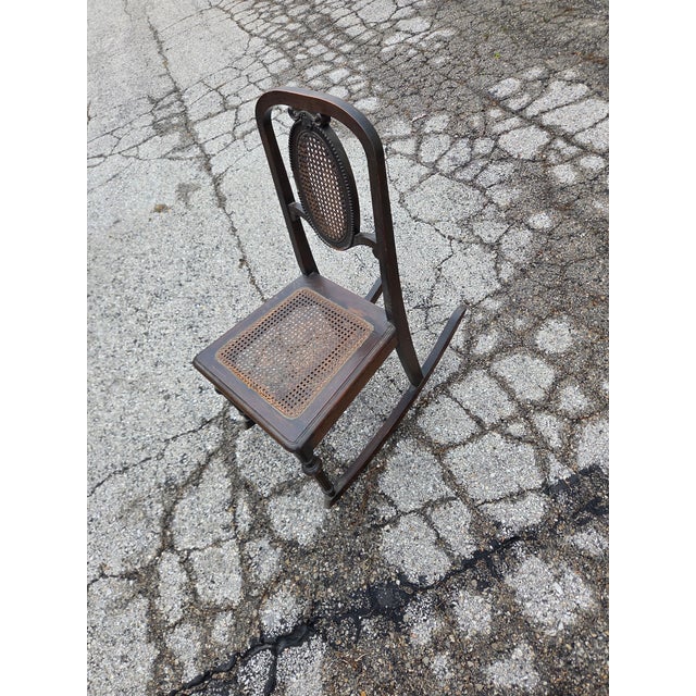 This is an antique dark brown wooden Victorian-style rocking chair featuring a woven cane seat and back. Some slight wear,...