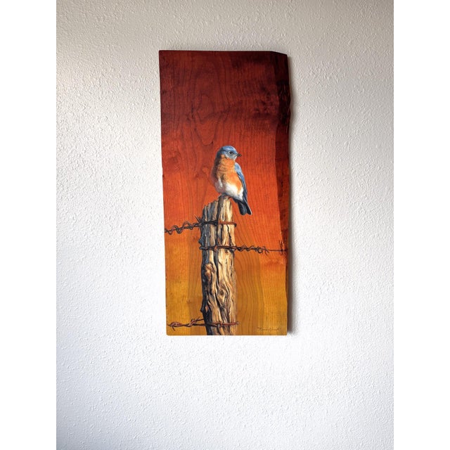 This artwork depicts a solitary bluebird perched on a weathered wooden post, set against a vibrant gradient of warm...