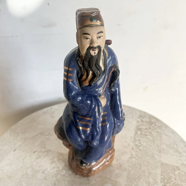 This vintage Chinese porcelain figurine depicts a traditional wise man rendered in a serene, contemplative pose. Glazed in...