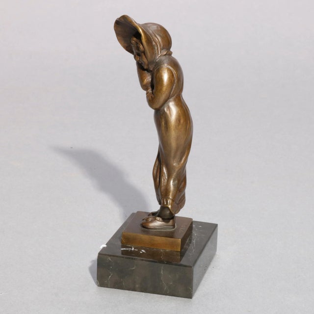 An antique figural child cast bronze sculpture depicts portrait of young girl Antique in hat, seated on marble base, circa...