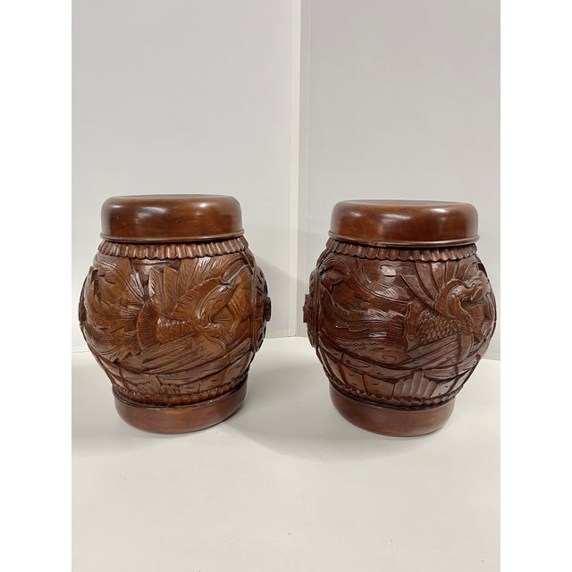 A pair of hand carved wooden hollow barrel-form garden stools in a warm reddish-brown finish with removable tops, a flat...