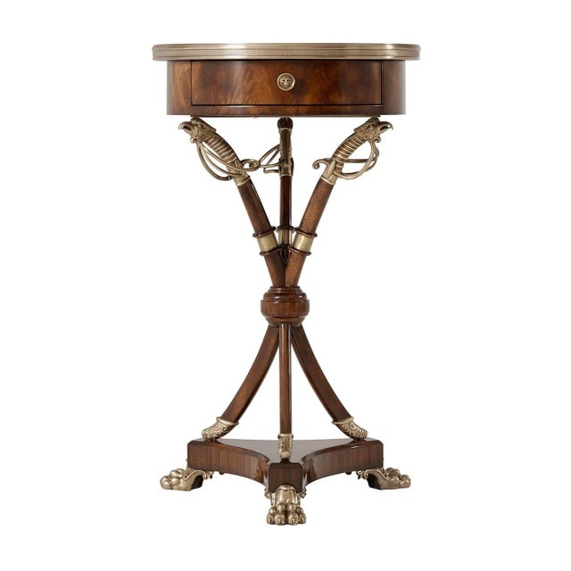 A Regency style mahogany side table, the circular brass bound top fitted with a frieze drawer on three bound brass hilted...