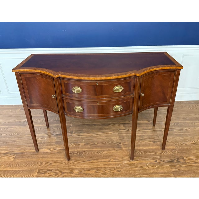 This is a 56 inch wide Hepplewhite Mahogany Sideboard by Leighton Hall. It features a classic serpentine shaped front,...