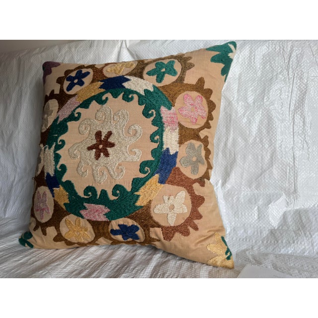 A decorative pillow created from a 1900s hand-embroidered Suzani textile, featuring a bold central medallion encircled by...