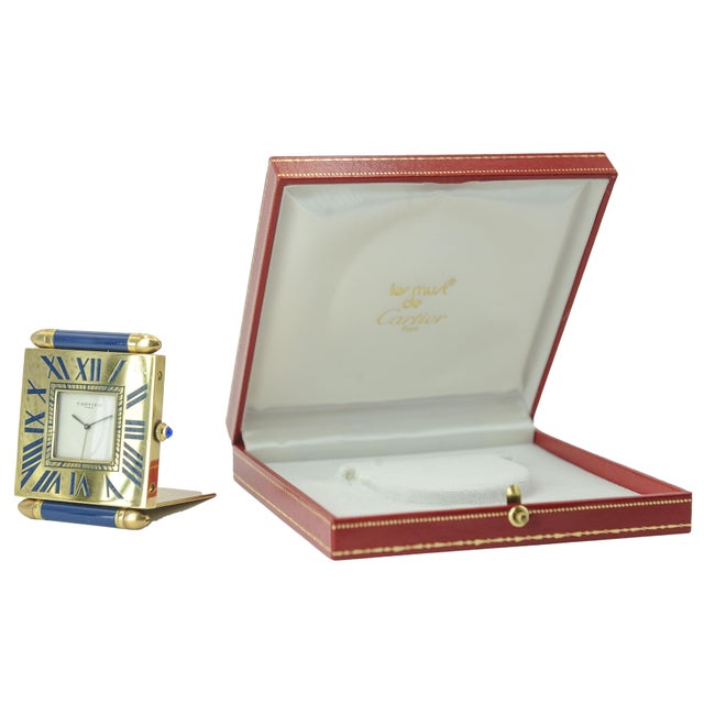 A beautiful cartier alarm clock in a gilded folding case with a signed cartier quartz movement and distinctive sapphire...