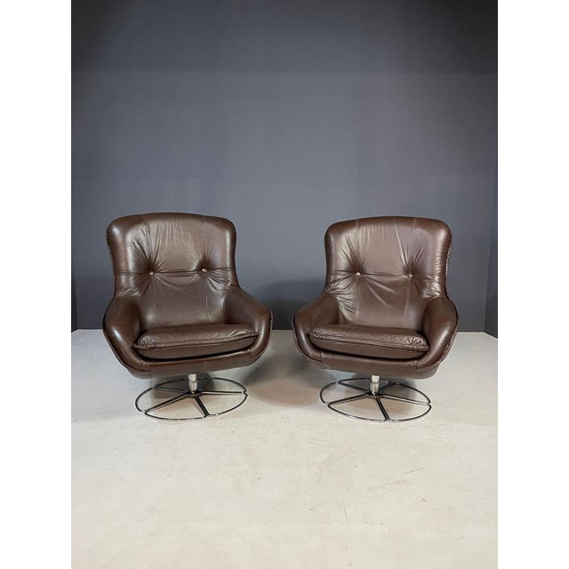 A pair of elegant swivel armchairs manufactured by peem in finland in the 1970s. Featuring original brown leather...
