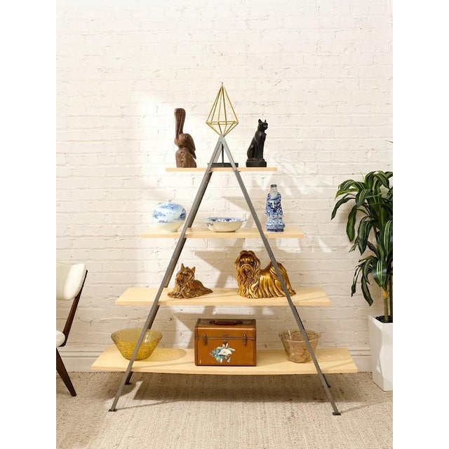 A striking open display shelf with an architectural A-frame silhouette, pairing warm natural wood shelves with a slender...