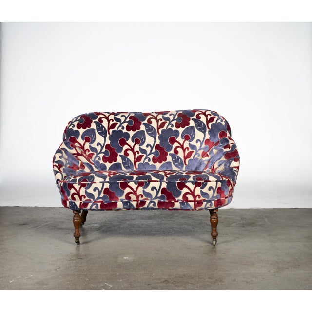 Vintage upholstered settee featuring a rounded-back silhouette, turned wood legs, and vibrant patterned textile.