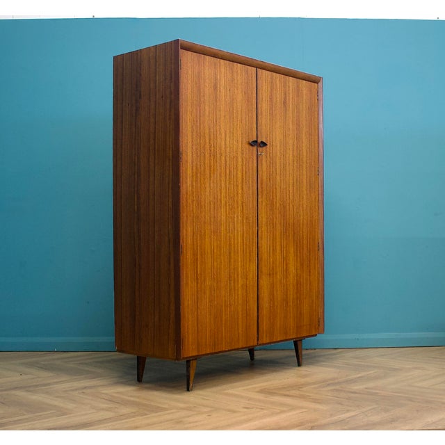 Mid-century wardrobe crafted in warm-toned wood with a clean, minimalist silhouette. Featuring beautifully grained doors,...