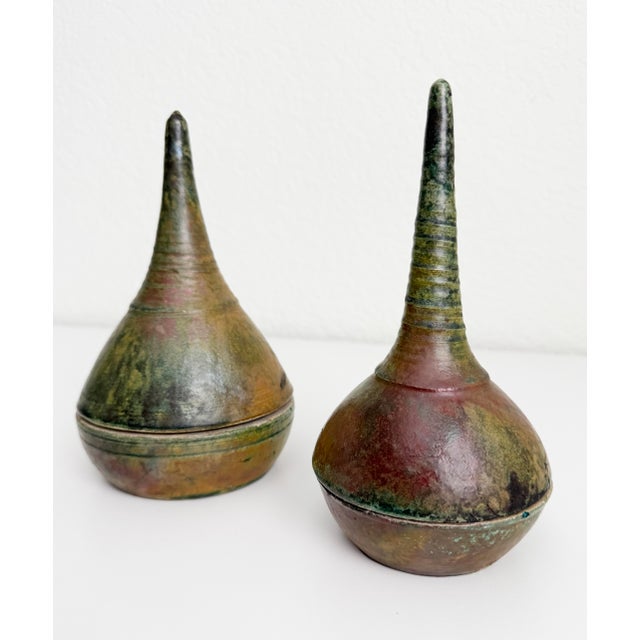 A pair of unique lidded vessels made of raku-fired earthenware. Each features a sculptural, elongated handle and organic...