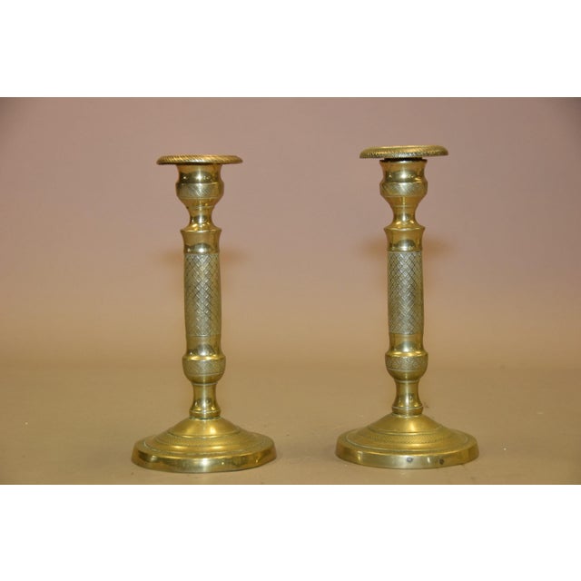 Pair of French bronze candlesticks dating to circa the 1910s. Each has a round stepped base, a column decorated with a...