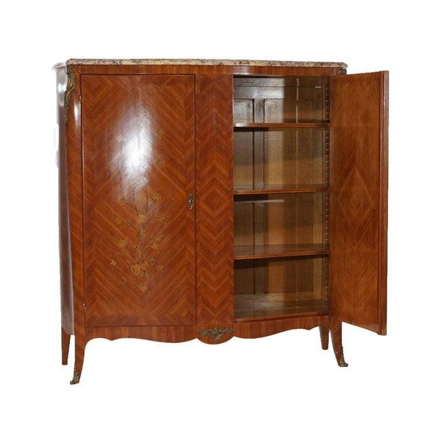 An antique French armoire offers shaped marble top over bookmatched Kingwood case having double doors, floral satinwood...