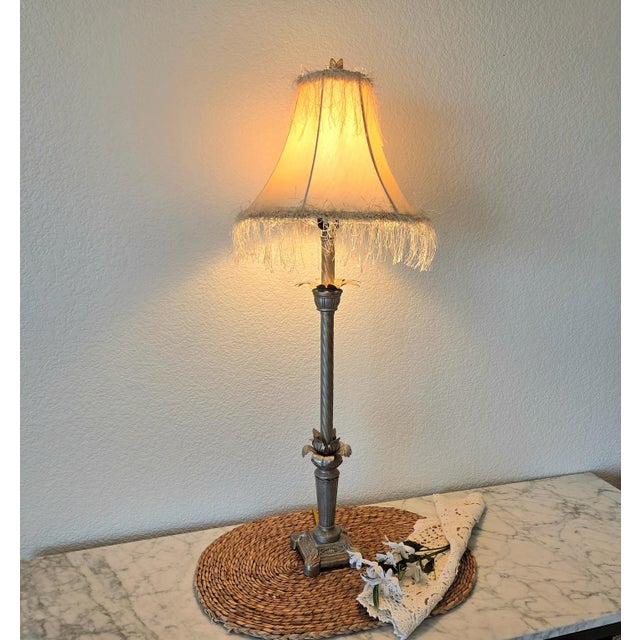 Elegant table lamp featuring a silver metallic finish paired with a soft beige bell-shaped fabric shade with decorative...