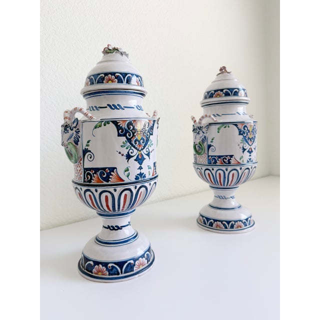 This pair of French, hand-painted ceramic urns was produced in the mid-20th century and styled after 19th-century French...