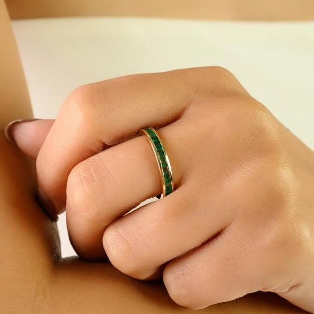 This elegant band ring features 14 natural square-cut emeralds with a total weight of approximately 0.67 carats,...