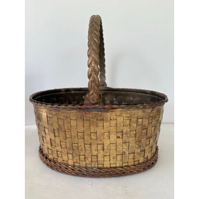 This vintage woven brass basket features a beautifully crafted oval form with a twisted brass handle and braided rim and...