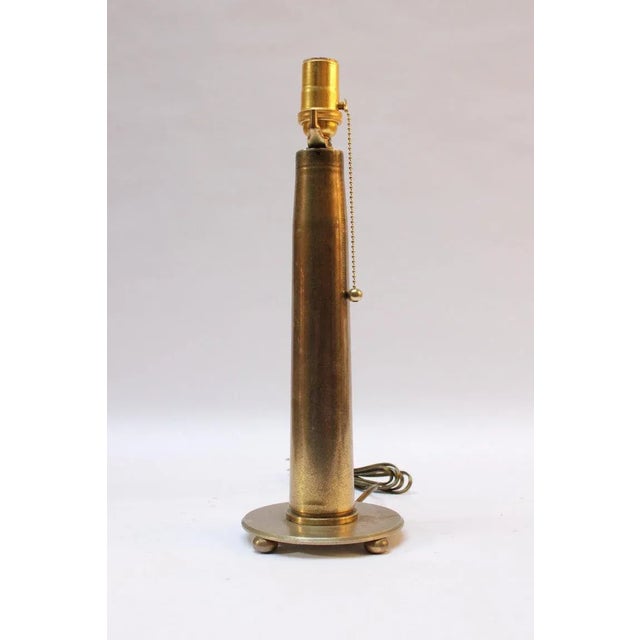Circa 1930s Trench Art Lamp fashioned from a brass artillery shell mounted to a brass base supported by three ball feet....