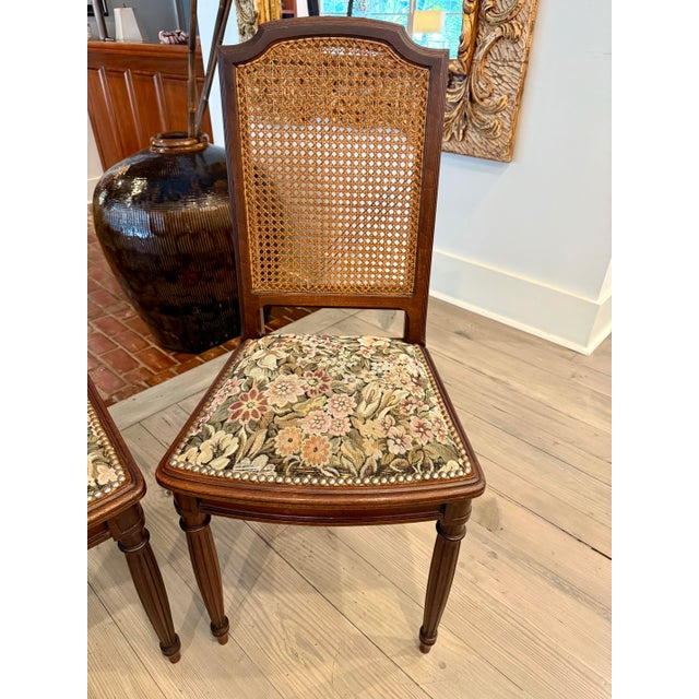 Imported French Louis XVI walnut cane back dining chairs with floral tapestry upholstery and nail head trim. These chairs...